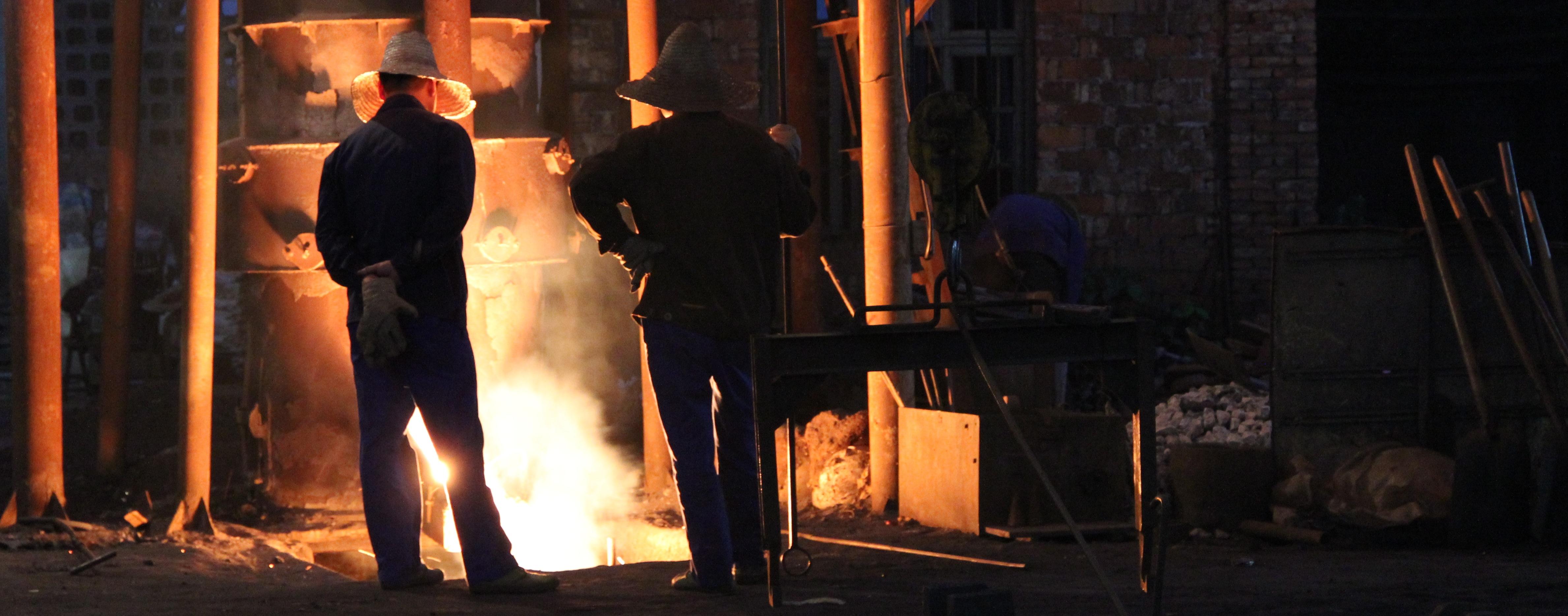 Two people overlook hot molten iron in a foundry.