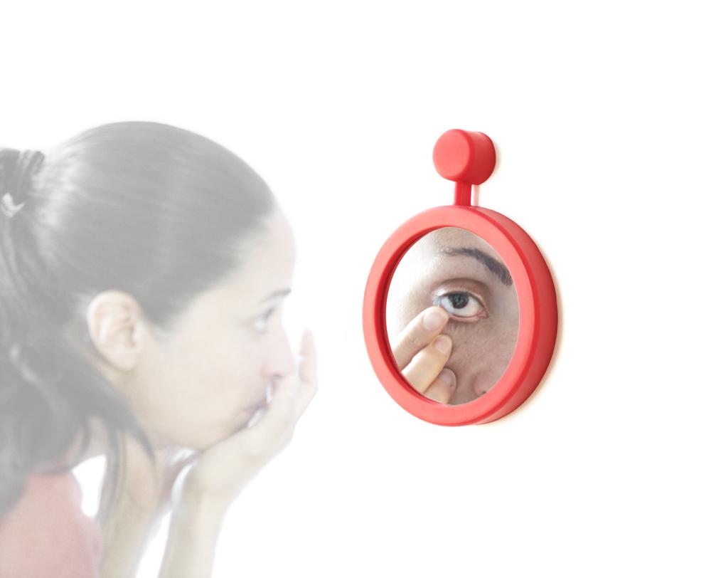 A photo of a woman looking into a red-border mirror.