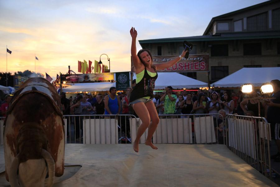 A woman jumps in the air next to a mechanical bull.