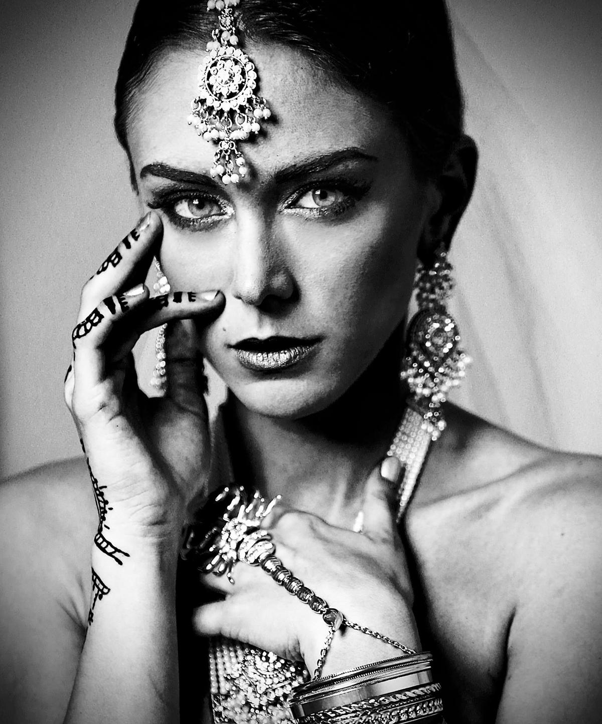 A straight-on black-and-white portrait of a woman decked in jewelry.