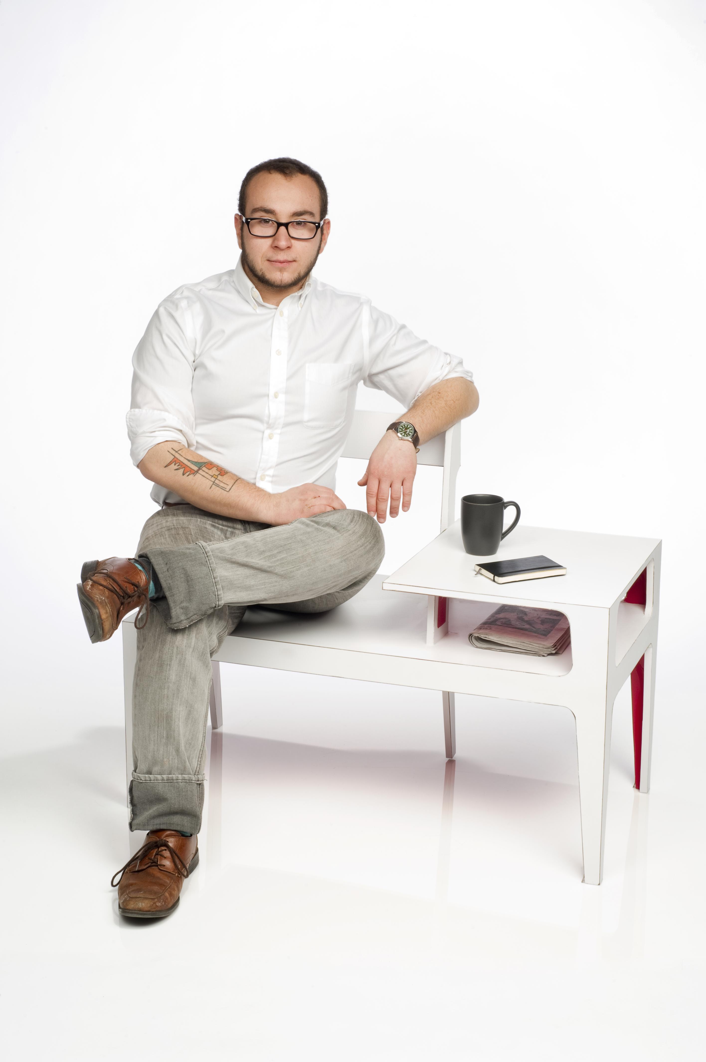 A person sits on a chair-desk hybrid design, resting his coffee and phone on the surface.