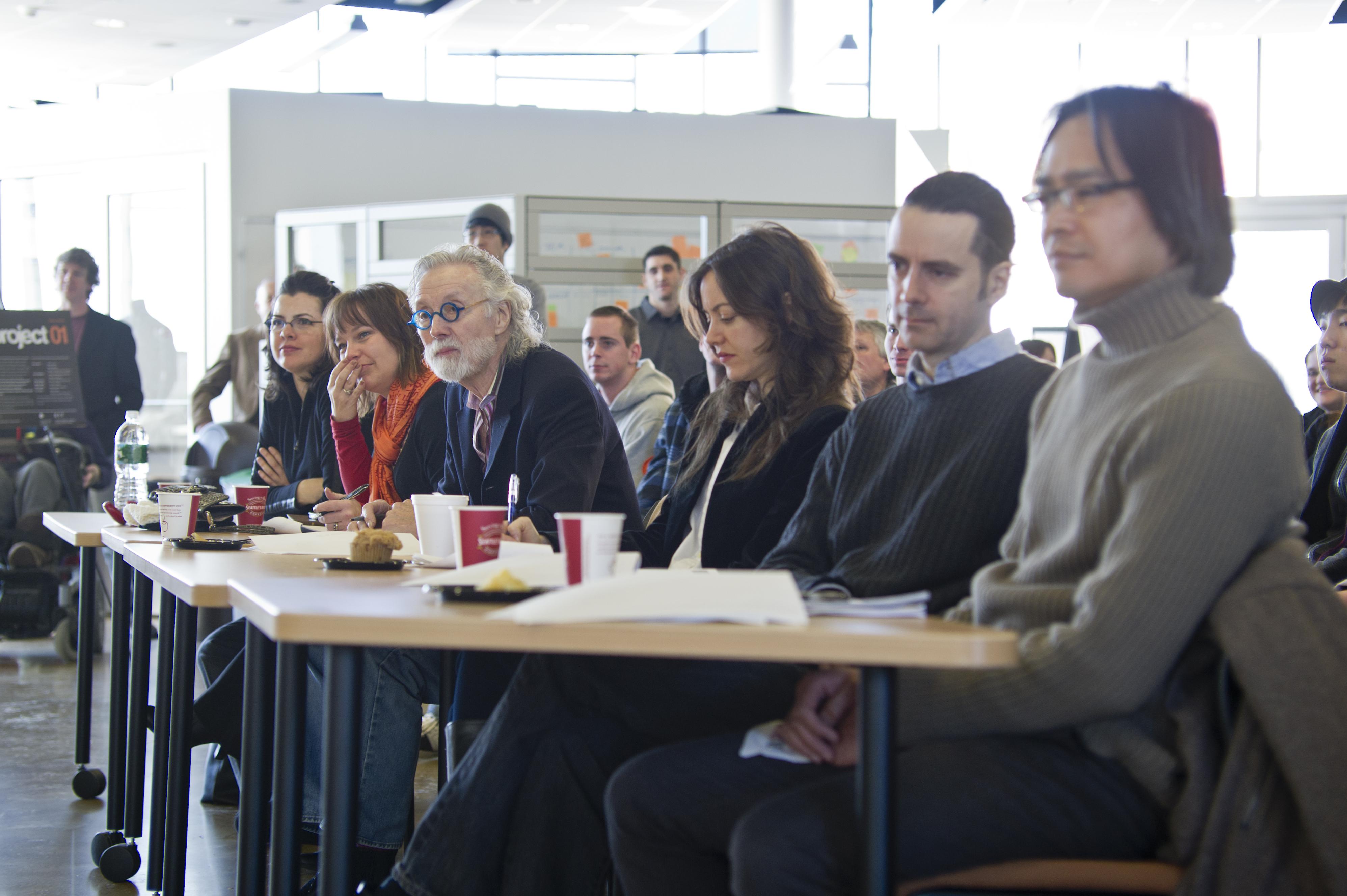 A group of people sit together at a table, judging seat designs.