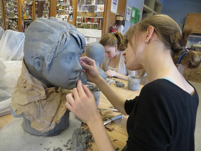 A student carving a clay face.